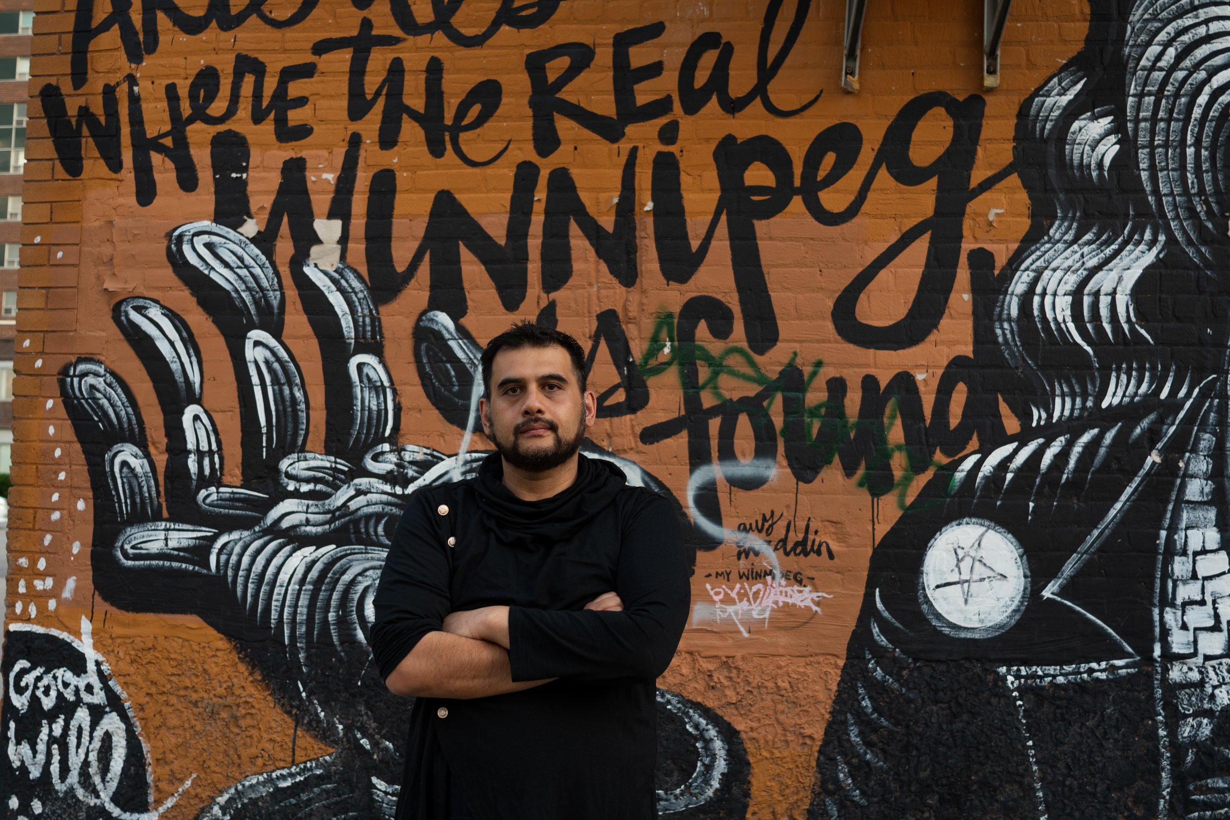 Omar Kinnarath in front of mural with text : The Real Winnipeg Is Found